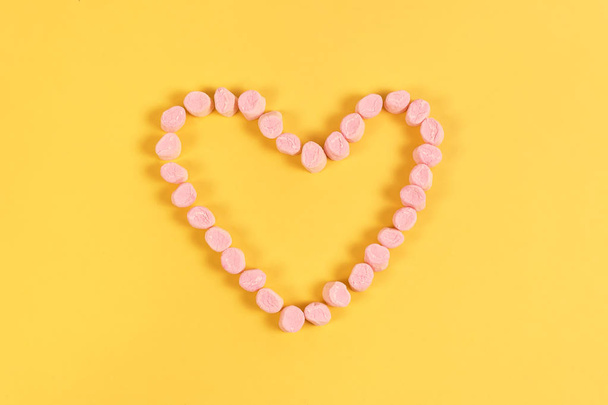 dulces de malvavisco colocados en forma de corazón.El día de San Valentín y el concepto de amor sobre fondo amarillo
 - Foto, imagen