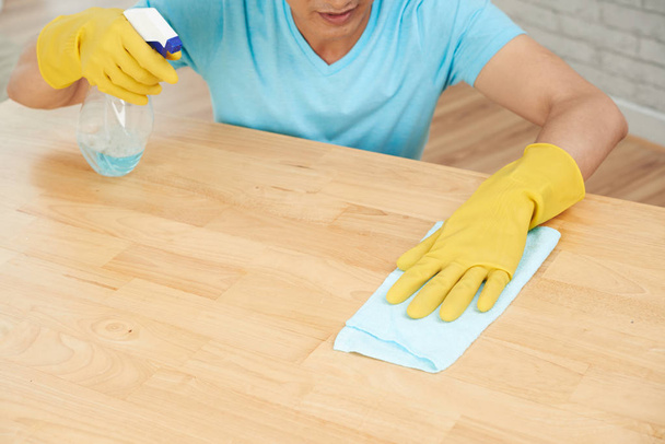 Man spraying and wiping wooden table surface - Foto, immagini