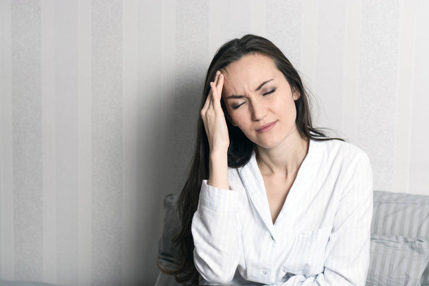 Portrait d'une jeune brune en pyjama assise au lit, maux de tête, migraine
 - Photo, image