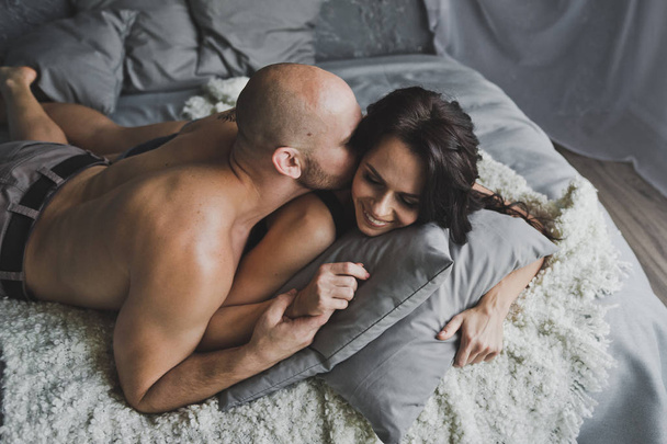 Bald brutal man kisses the cheek of the girl on the bed 127. - Fotoğraf, Görsel