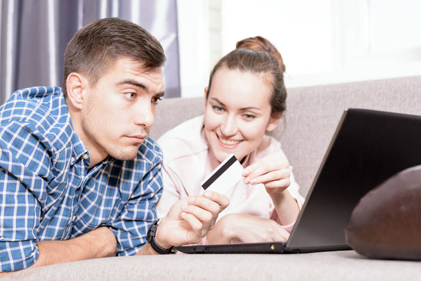 Moderni nuori perhe tekee ostoksia verkossa Leda sohvalla kannettavalla tietokoneella, maksu luottokortilla. Emotionaaliset kasvot
 - Valokuva, kuva