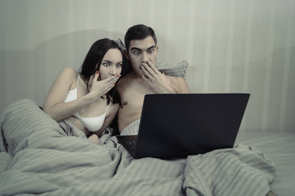 Fiatal családi pár használ laptop és filmnézéshez az ágyban. horror film - Fotó, kép