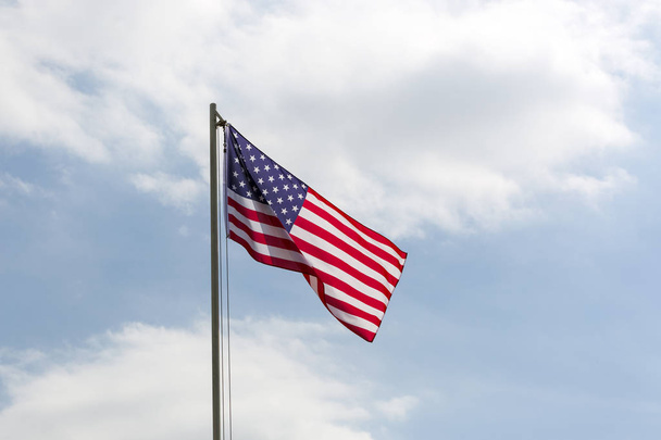 Bandeira dos Estados Unidos em um mastro de bandeira na frente do céu azul
 - Foto, Imagem