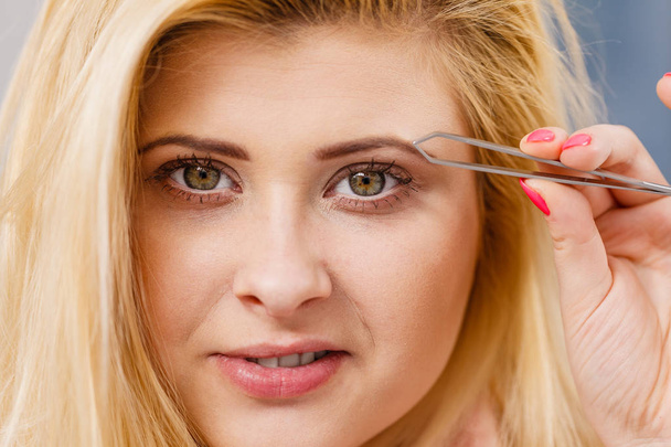 Woman tweezing eyebrows depilating with tweezers - Foto, Bild