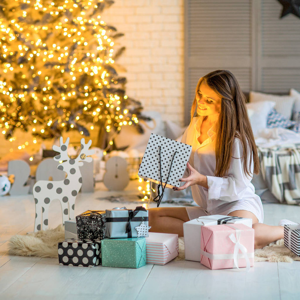 Dziewczyna, w domu na Boże Narodzenie, patrząc na prezenty pod tre Boże Narodzenie - Zdjęcie, obraz