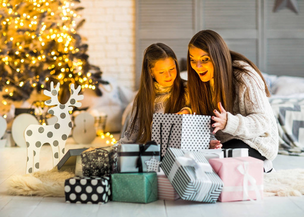 Young mother and her ittle daughters opening a magical Christmas - Фото, изображение