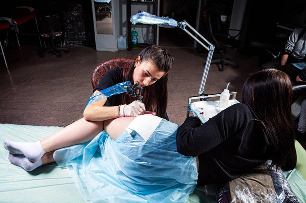 Mujer morena tatuaje maestro haciendo tatuaje de un pequeño pájaro de la teta en las caderas con tatuajes rojos en una joven mujer tatuaje en un salón de tatuajes
 - Foto, imagen