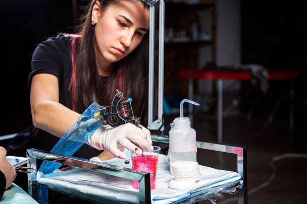 Νεαρή γυναίκα τατουάζ πλοίαρχος κόκκινη μπογιά προετοιμάζει για ένα τατουάζ μηχανή πληρώσεως - Φωτογραφία, εικόνα