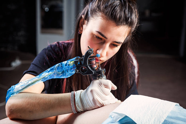 Tatuaje haciendo por artista profesional es tatuar a la mujer del cuerpo utilizando la máquina en un estudio de trabajo de diseño creativo
 - Foto, Imagen
