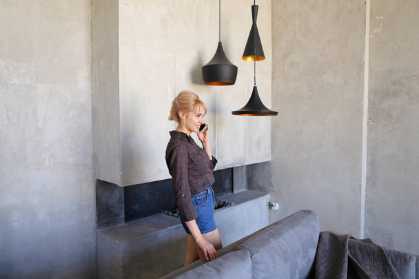 Vrouwelijke blonde spreekt op mobiele en loopt rond woonkamer, s - Foto, afbeelding