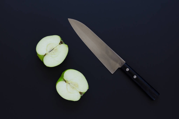 Two halves of green apple and knife on black background - Foto, imagen