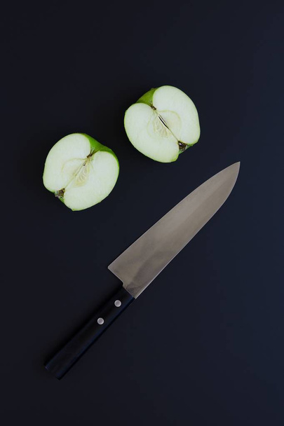 Two halves of green apple and knife on black background - Photo, Image