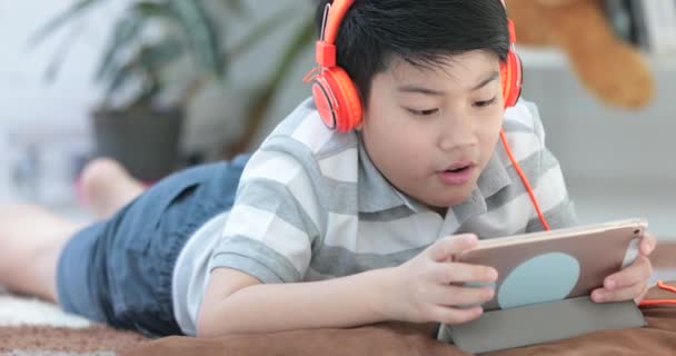 Close up de asiático pré-adolescentes descansar no chão e jogar tablet computador com sorriso rosto em casa
. - Filmagem, Vídeo