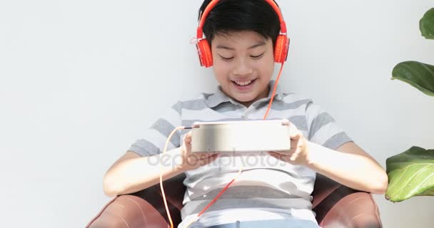 Azjatycka młodzież gry komputer typu tablet z uśmiechem twarz w domu. - Materiał filmowy, wideo