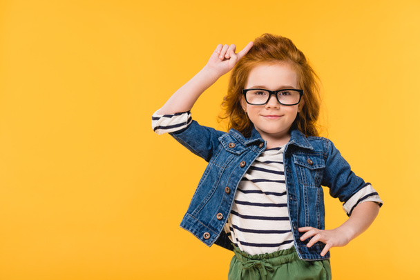 portrait of cute little kid in eyeglasses standing akimbo isolated on yellow - Foto, Imagem