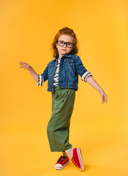 cute little kid in eyeglasses dancing isolated on yellow - Foto, Imagem