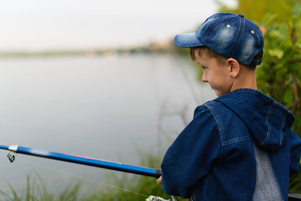 A fisherman boy on the river bank with a fishing rod in his hand - Photo, Image