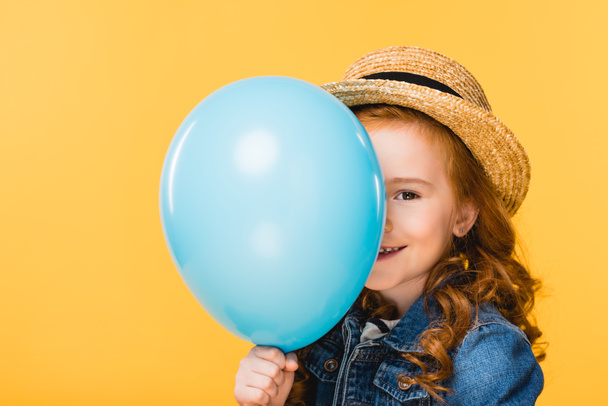 verdeckter Blick auf lächelndes Kind, das Gesicht mit Luftballon auf gelbem Grund verdeckt - Foto, Bild