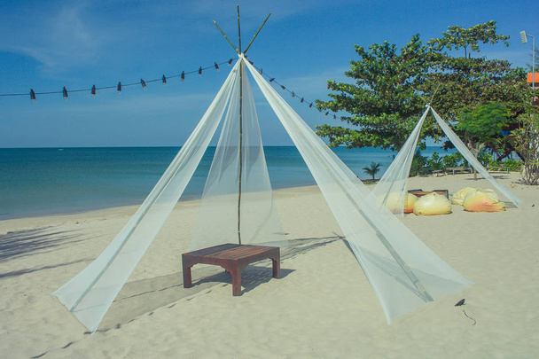 Cadeira de plataforma de madeira em pavilhão branco na praia de areia com bela vista da paisagem marinha e céu azul no fundo
. - Foto, Imagem