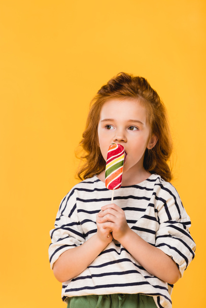 portrait of preteen child eating lollipop isolated on yellow - Zdjęcie, obraz