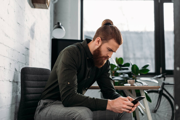 handsome businessman sitting and looking at smartphone - Foto, afbeelding