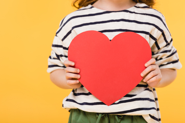 partial view of kid with red paper heart in hands isolated on yellow, st valentines day concept - Photo, Image