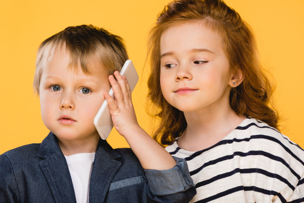 portrait of little boy talking on smartphone with friend near by isolated on yellow - Foto, Imagen