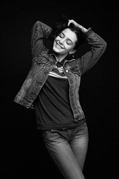 Beautiful young brunette woman in denim clothes posing against dark studio background - Zdjęcie, obraz