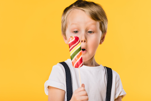 selective focus of adorable little boy with lollipop in hand isolated on yellow - 写真・画像