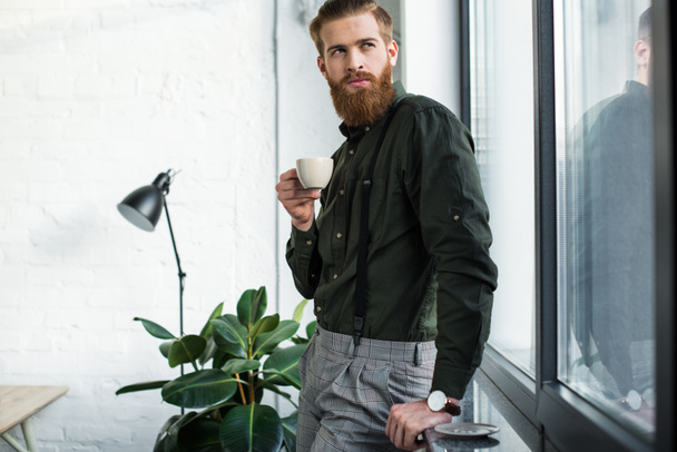 bearded businessman standing with cup of coffee and looking away - Foto, afbeelding
