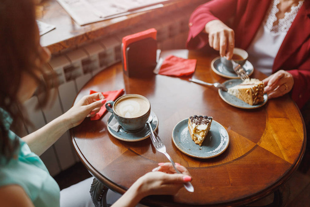 Two women chatting in a coffee shop, cake on the table - Foto, imagen