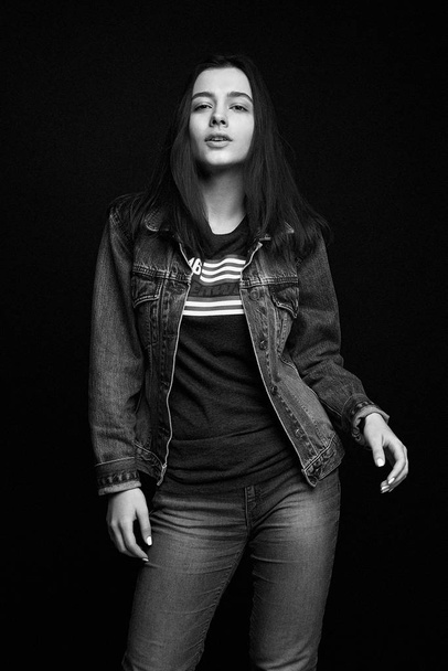 Beautiful young brunette woman in denim clothes posing against dark studio background - Fotó, kép