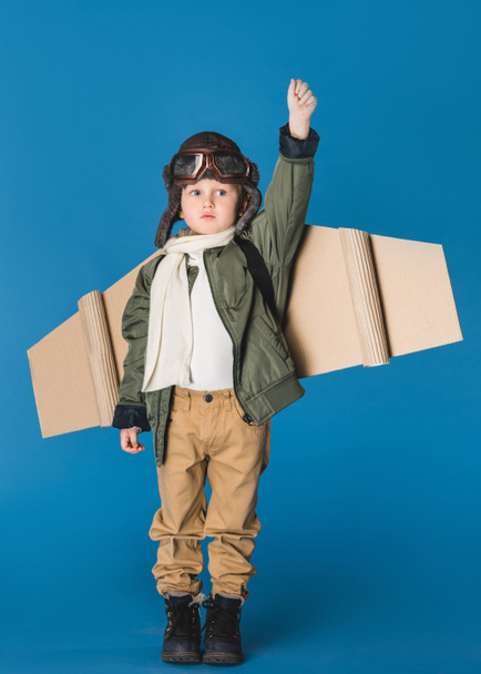 cute little boy in pilot costume with paper plane wing isolated on blue - Photo, image