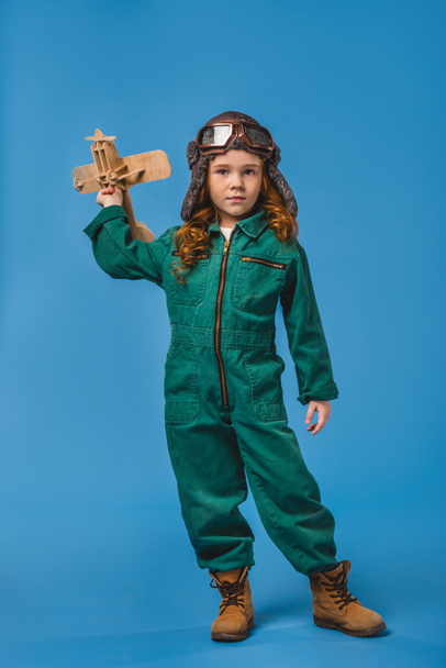 adorable child in pilot costume with wooden plane toy isolated on blue - Foto, afbeelding