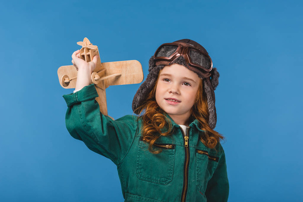 portrait of adorable child in pilot costume with wooden plane toy isolated on blue - Fotografie, Obrázek