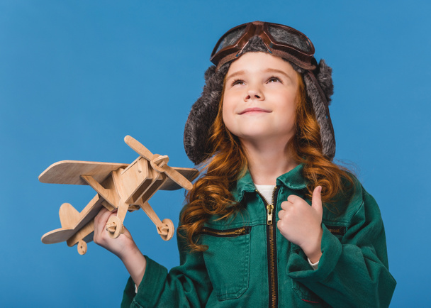 retrato de niño sonriente en traje de piloto con juguete plano de madera aislado en azul
 - Foto, Imagen