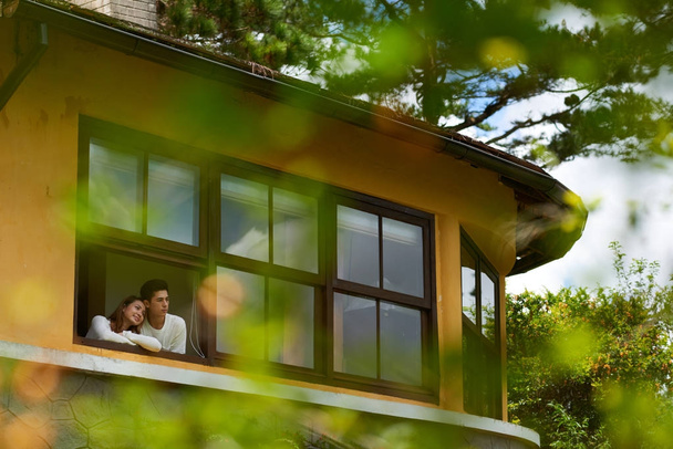 Beautiful Asian couple looking out of window of their house on early autumn day - Photo, Image