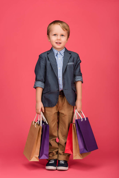 cute little boy with shopping bags in hands isolated on pink - Photo, Image