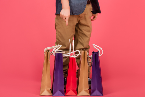 částečný pohled dítě ukazuje na nákupní tašky izolované na růžové - Fotografie, Obrázek