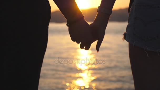 Silhouette of male and female hands holding each other at sunset against an sea background. Young couple joining arms outdoor. Concept of loving and happiness. Close up Rear back view Slow motion - Footage, Video
