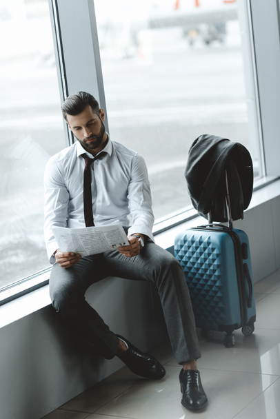 knappe zakenman krant lezen tijdens het wachten voor de vlucht op de luchthaven lobby - Foto, afbeelding