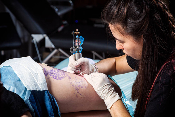Közelről, professzionális tetoválás művész teszi egy tetoválás a combcsont - Fotó, kép