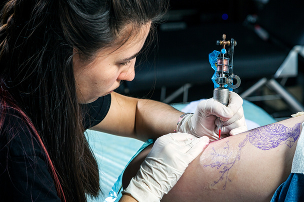 Close up of professional tattoo artist makes a tattoo on the femur - Photo, Image