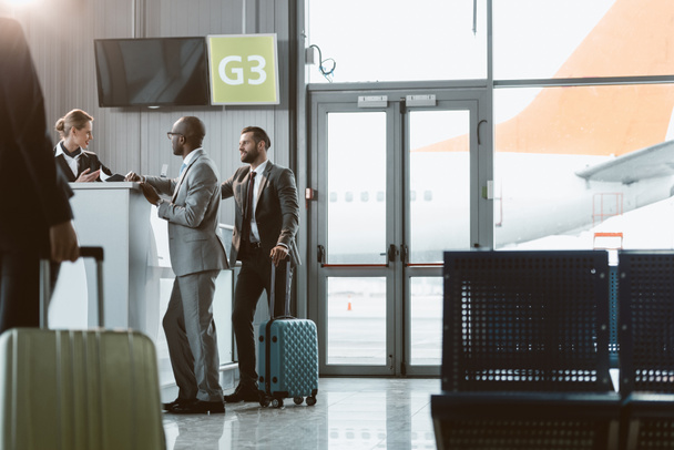 businessmen standing at airport reception to buy tickets while colleague walking to them - Photo, Image