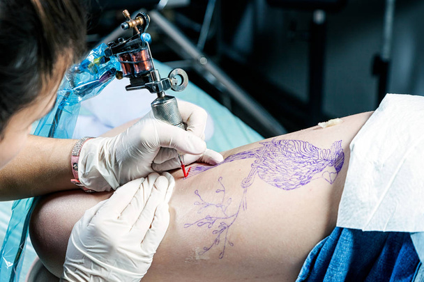 Mujer tatuadora mostrando el proceso de hacer un pájaro tatuaje en la mujer. Diseño del tatuaje en patrón
 - Foto, Imagen