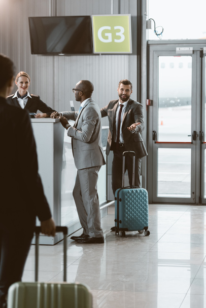 businesspeople standing at airport reception to buy tickets while colleague walking to them - Foto, Imagen