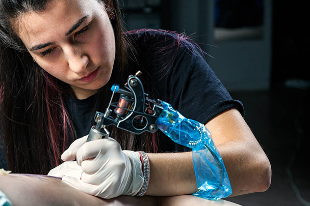 Επαγγελματική τατουάζ καλλιτέχνης κάνει μια δερματοστιξία σχετικά με το μηριαίο οστό - Φωτογραφία, εικόνα