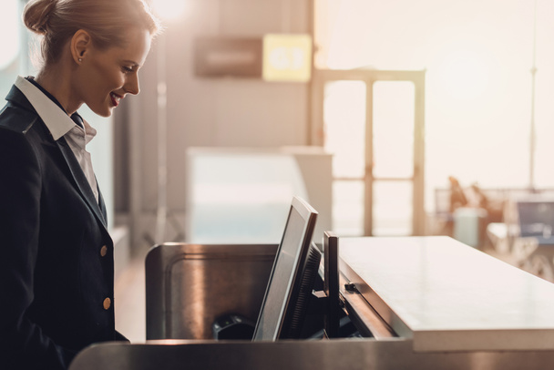 боковой вид привлекательного молодого работника аэропорта на рабочем месте у стойки регистрации в аэропорту
 - Фото, изображение