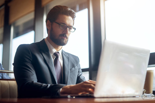 exitoso joven hombre de negocios barbudo guapo en traje de trabajo con el ordenador portátil en la cafetería
 - Foto, Imagen