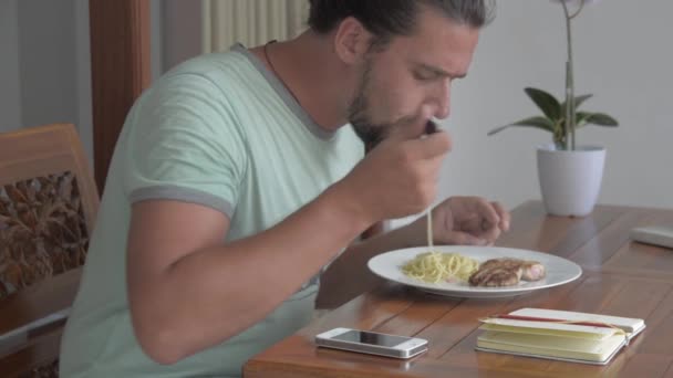 Young man using phone while eating breakfast - Video